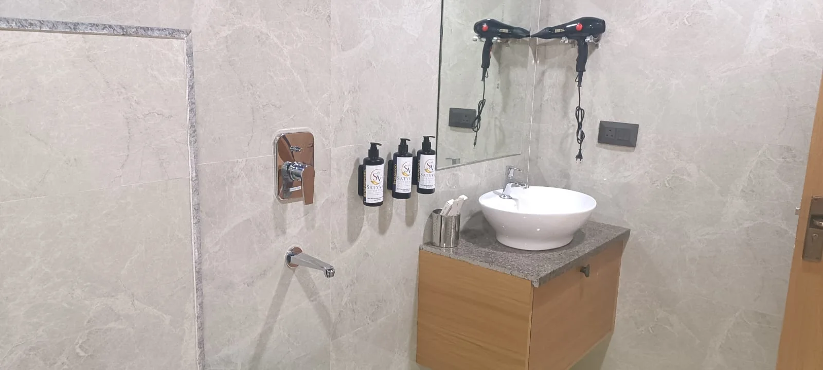 Spacious guest room  at Satyvan Hotel Gwalior showing a smart TV, seating area, mini fridge, and wood furnishings