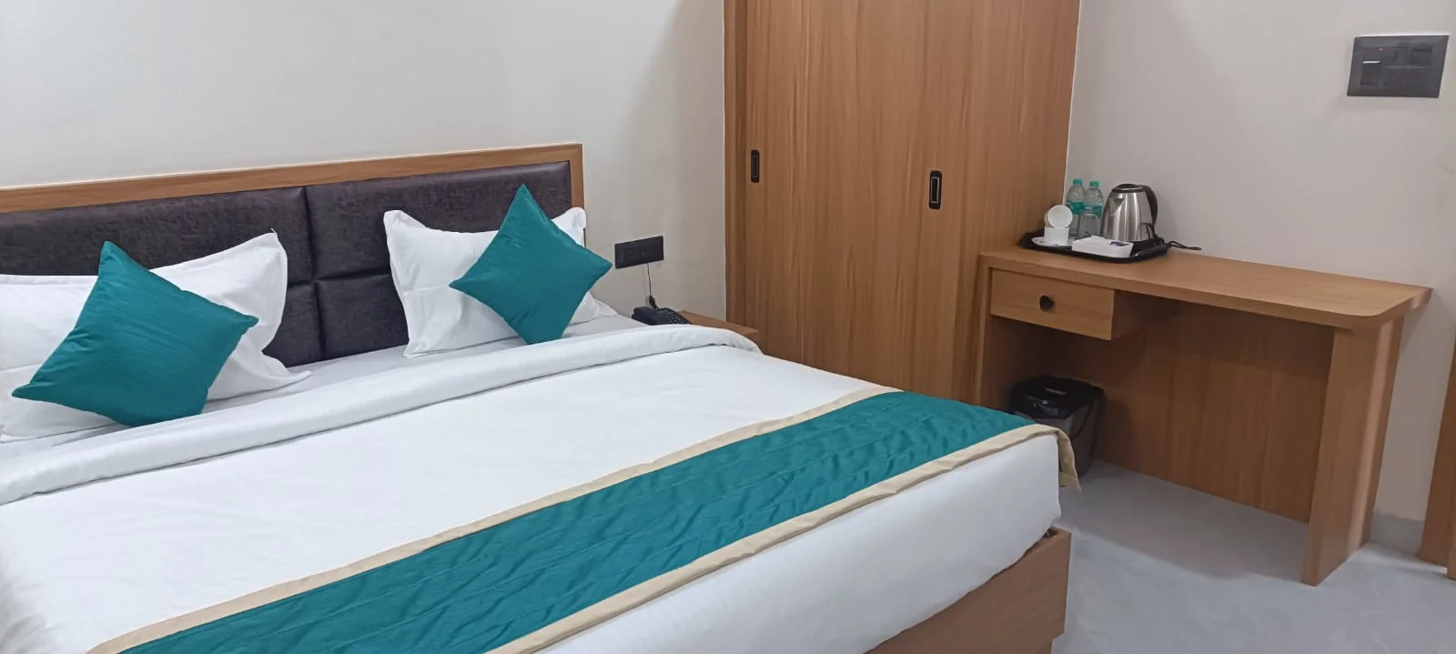Spacious guest room at Satyvan Hotel Gwalior with a smart TV, seating area, mini fridge, and wood furnishings