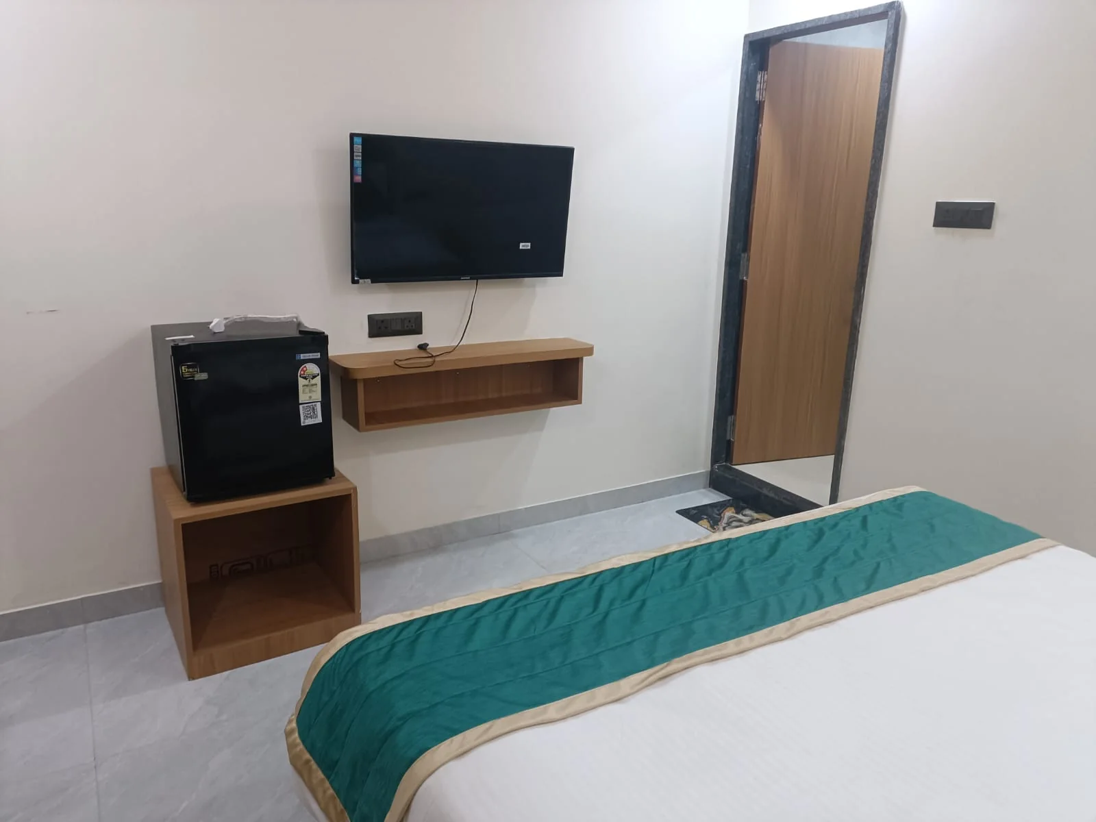 Spacious guest room at Satyvan Hotel Gwalior with a smart TV, seating area, mini fridge, and wood furnishings